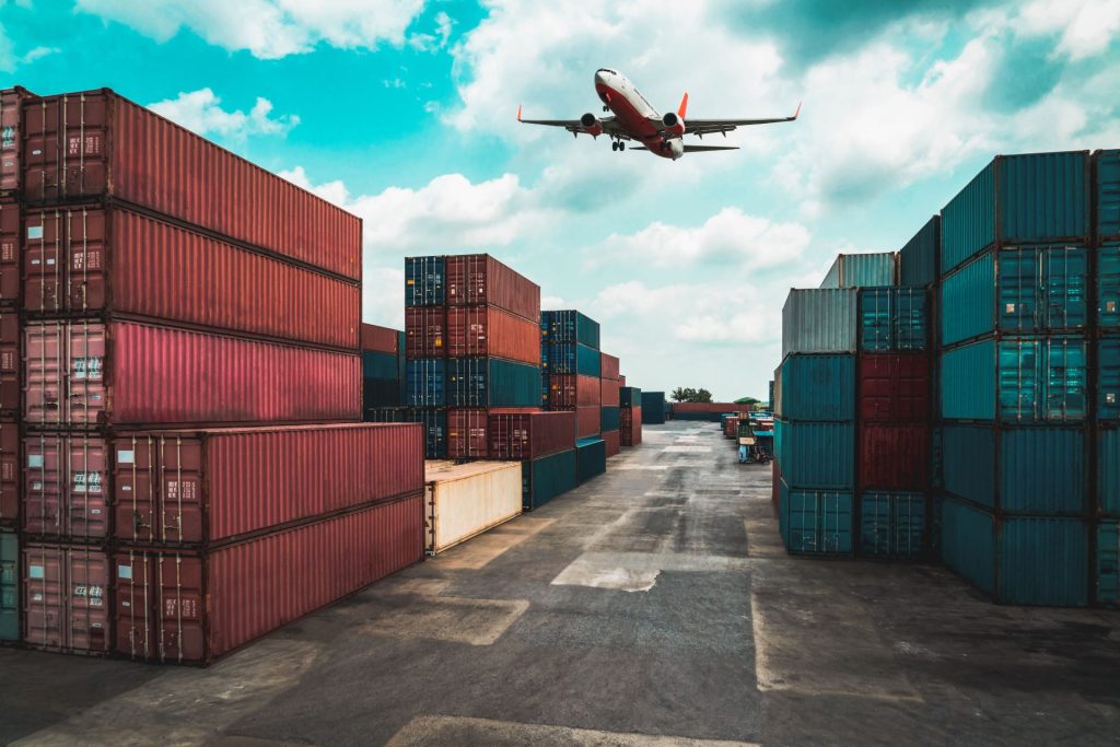 Avión sobrevuela un puerto comercial lleno de contenedores de mercancías